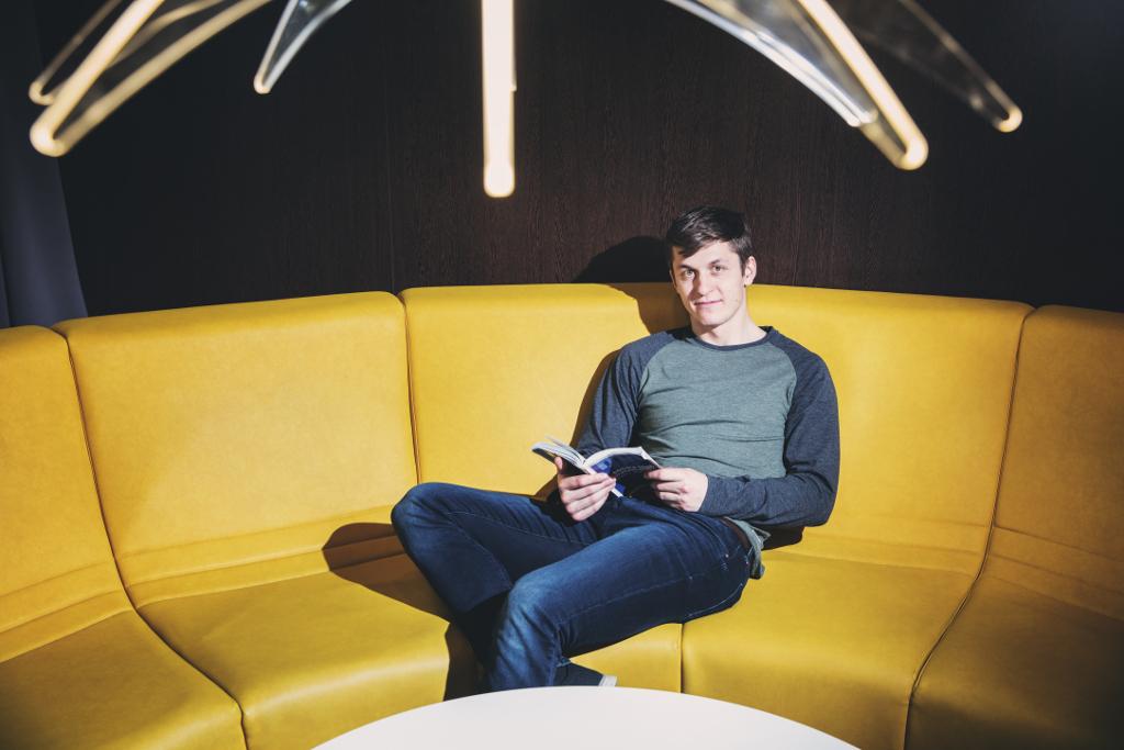 Lukáš Radil sedí na žlutém gauči s knihou
