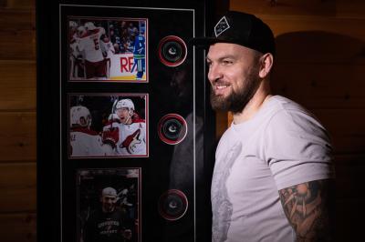 Martin Hanzal stojí u výstavky s fotkami a puky z NHL, na hlavě má kšiltovku, na ruce tetování