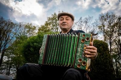 Jiří Císař sedí s harmonikou, za sebou má stromy